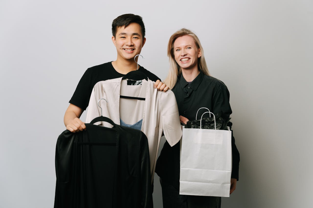 A happy couple displaying fashion choices with bags and clothes in a studio setting.