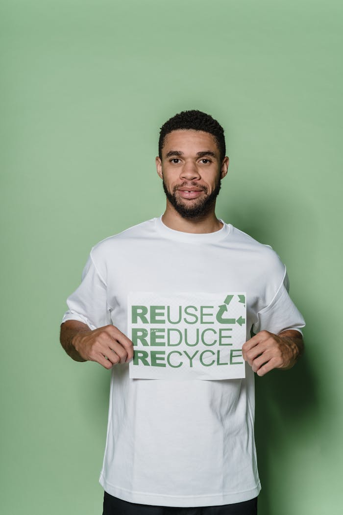 about-img Young adult holding a reuse reduce recycle sign against a green background, promoting environmental awareness.